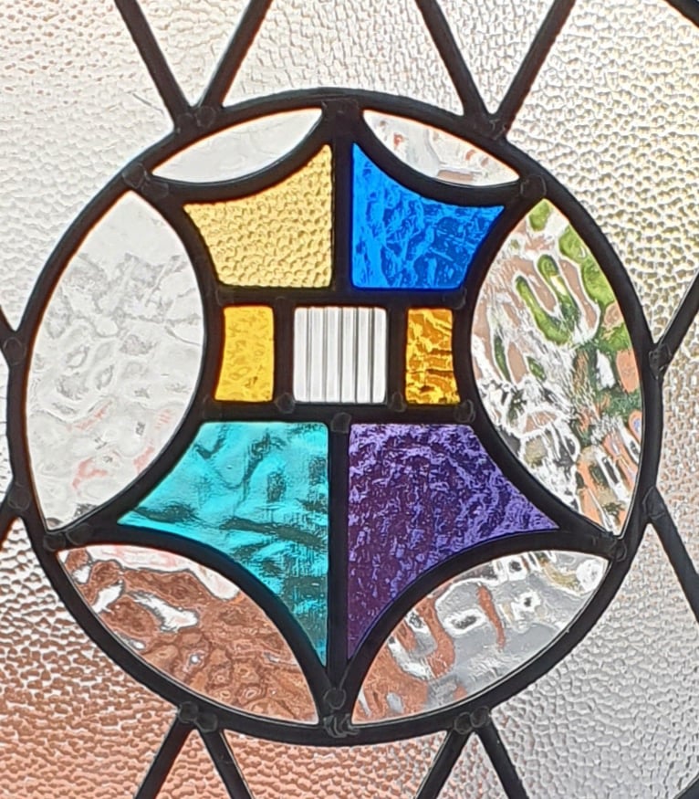 Bay window with decorative leaded glass being prepared for replacement, with tools on the sill and a residential street visible outside.