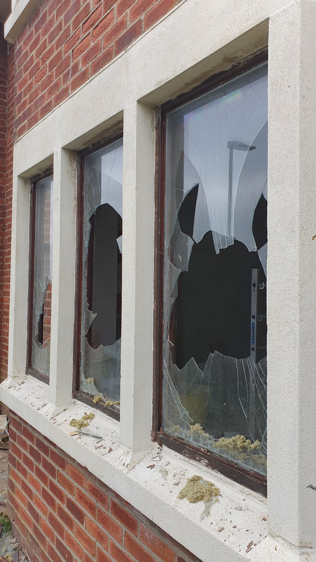 “Broken double‑glazed window with a large hole and shattered glass, with a Double Glazing Repairs service van visible outside.