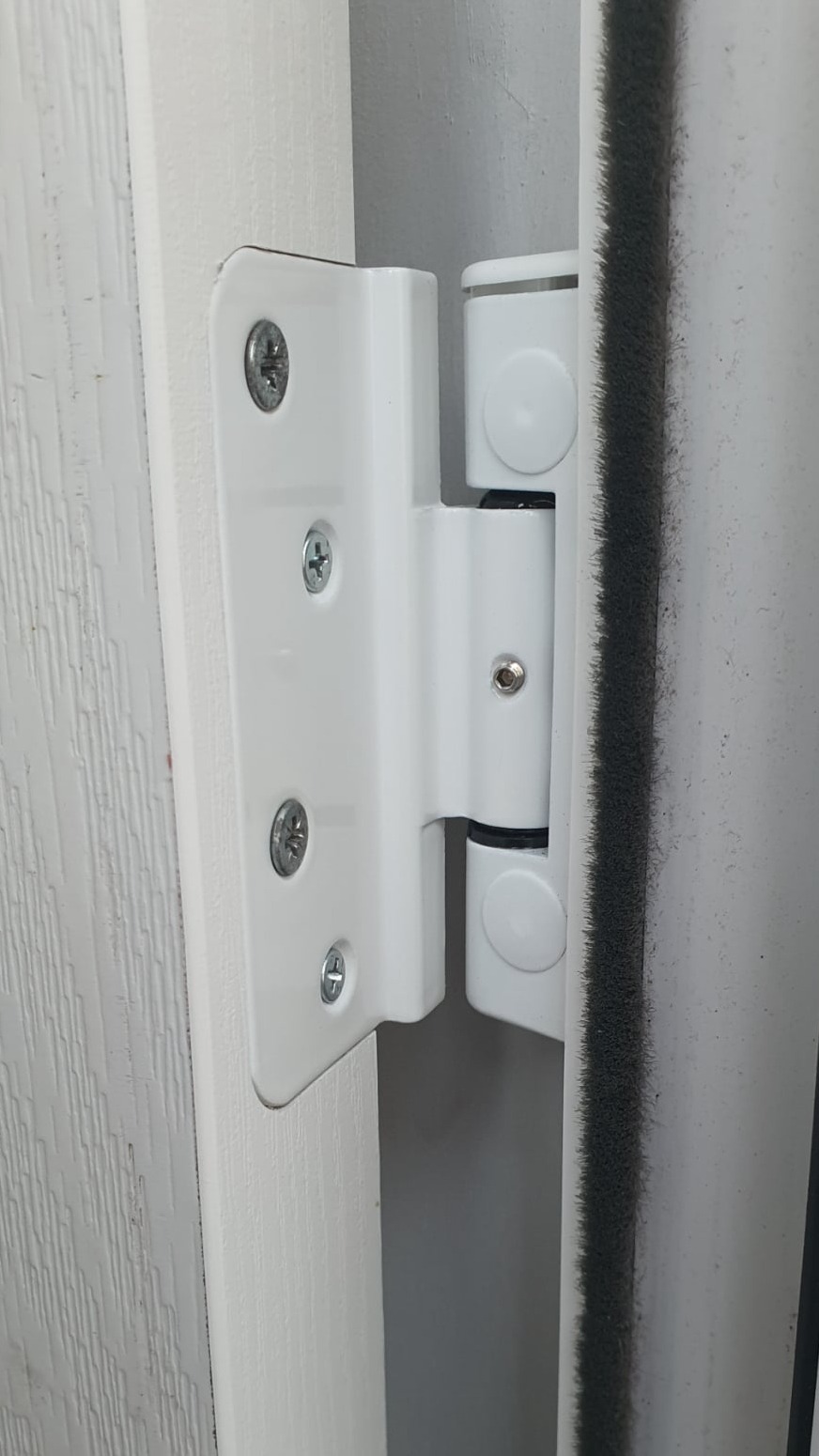 “Close‑up of a uPVC door hinge mechanism during repair, showing the metal friction stay, screws and corner buffer with tools visible in the background.