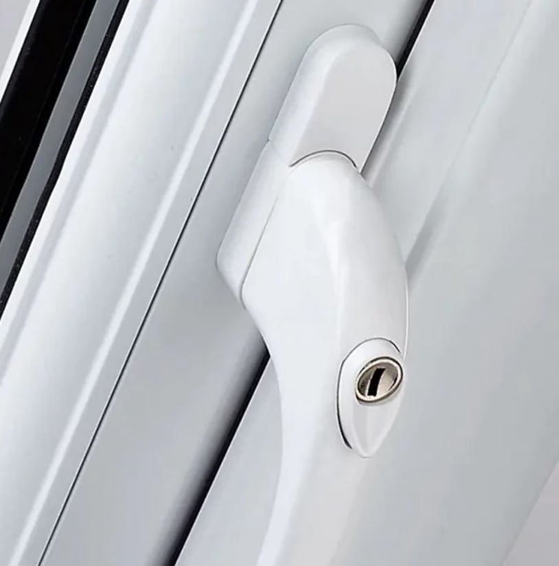 A close‑up of a white uPVC window handle with an integrated key lock, mounted on a white frame. The handle is shown in the closed position, with the keyhole visible beneath it.